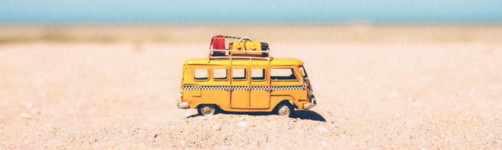 A yellow toy bus siting in the sand.